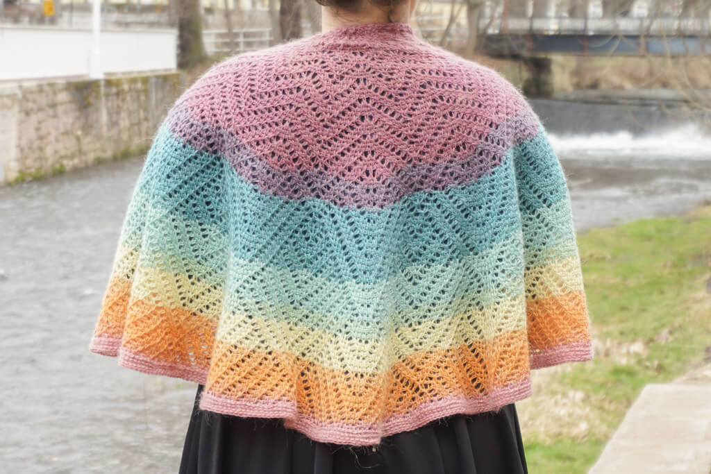 How to start a Tunisian crochet project in a magic ring 1 Back view of draped Tunisian crochet half circle shawl with lacy details and a progression of rainbow colors.