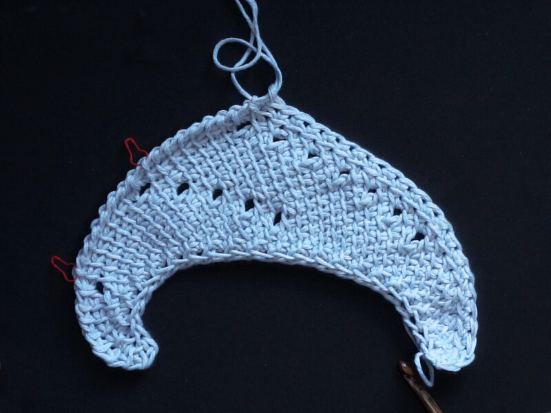 Tunisian crochet asymmetrical rounded triangle shawl tutorial 14 Tunisian Crochet kyanite shawl laid flat after one pattern repeat, showing 2 columns of eyelets going parallel with the right side, and the beginning of a new column of eyelets on the far left side.