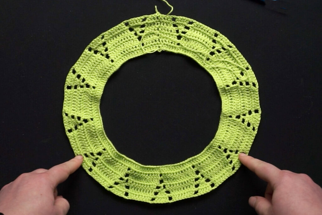 Lifting the back neckline of crochet round yokes 7 Full view of beginning of round yoke in double crochet stitches, with the back seam at the top and two hands pointing a third of the circumference away from the back seam on either side.