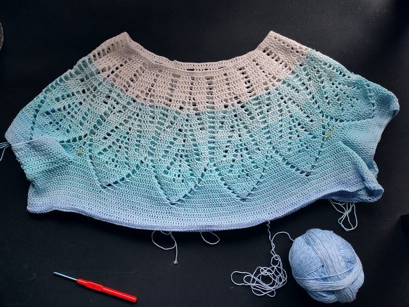 Project diary - Calliandra round yoke top 4 Partly completed round yoke top in white to light blue cotton gradient yarn. The yoke features lacy feathers that get wider towards the bottom and end in a plain fabric.