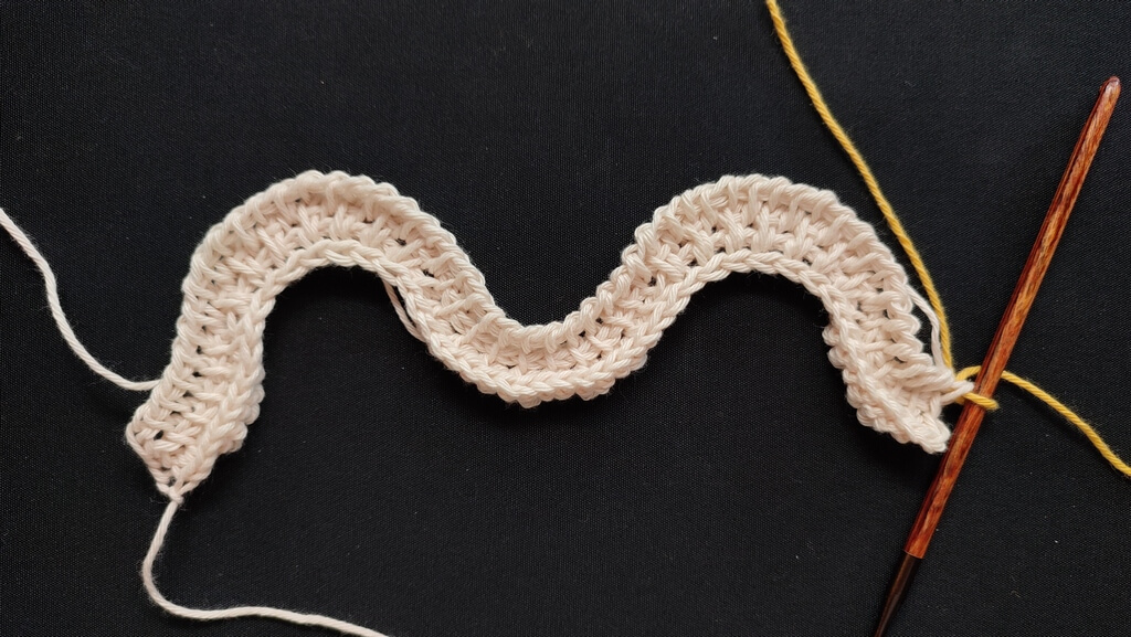 Feather and fan Tunisian crochet pattern for a washcloth 5 Three rows in beige cotton yarn of a feather and fan pattern, with the last row being of just plain stitches, without increases or decreases.
