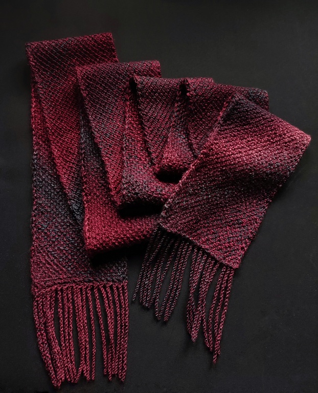 Corner to corner Tunisian crochet scarf pattern 1 Folded Tunisian crochet scarf, showing both the front and back of the fabric made on the bias, using acrylic yarn with sparkly threads and a quick changing gradient from dark pink to dark purple.