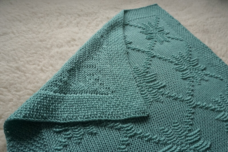 Nordic star Tunisian crochet baby blanket pattern 1 Front and back view of light teal baby blanket with a Nordic star Tunisian crochet stitch pattern made in smooth Tunisian knit stitches and raised Tunisian reverse stitches. The edging all around is made in honeycomb stitch.