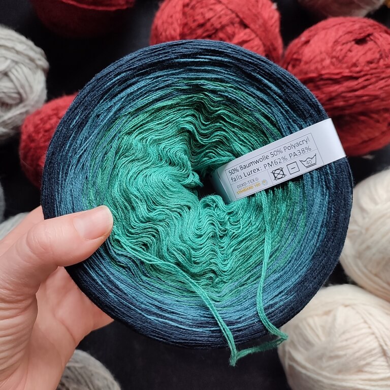 Large gradient yarn cake made of 4 colors, from a light teal blue to a dark petrol blue.
