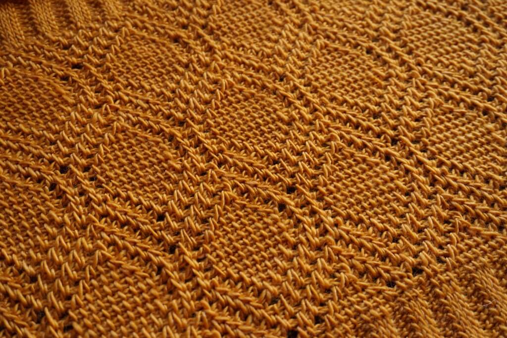 Close-up of Tunisian crochet lace in deep yellow yarn, showing a hexagonal pattern reminiscing of a honeycomb.